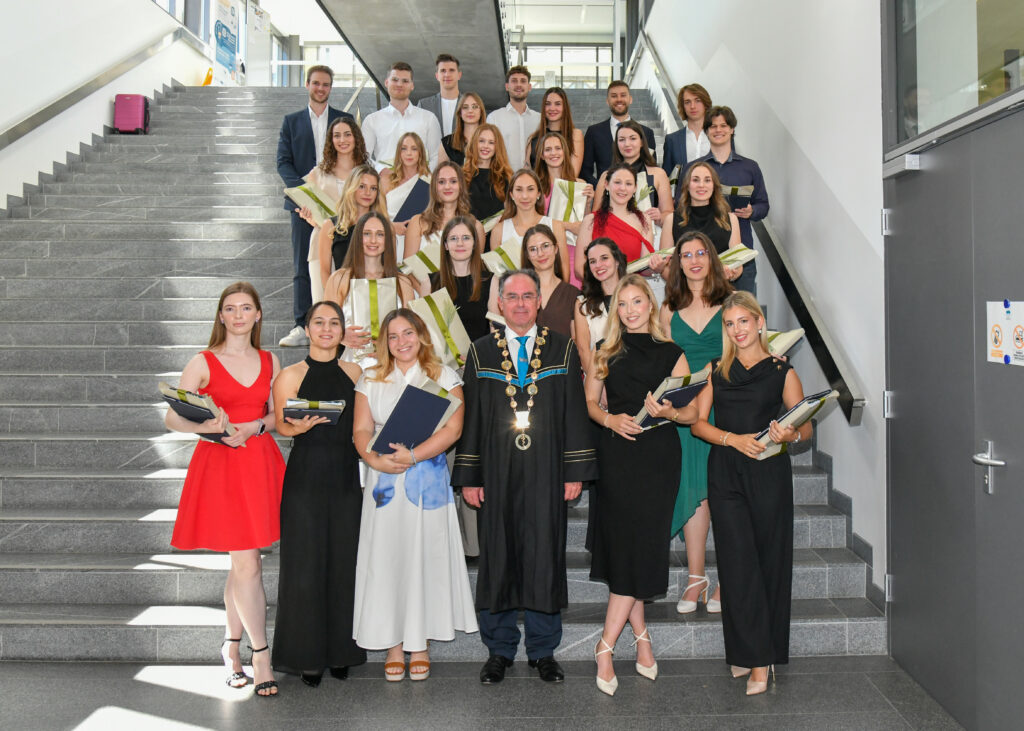 Skupinska fotografija diplomantov s šopki in vodstva na stopnišču. Podelitev diplom Medicinske fakultete UM 2026.