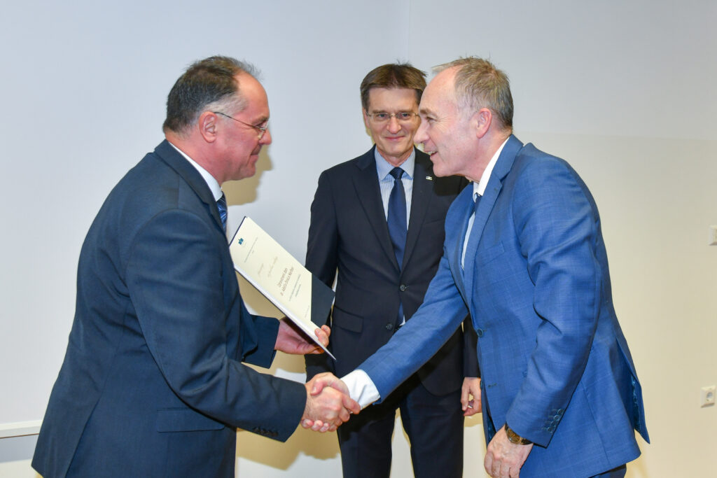 Dekan se rokuje s prejemnikom priznanja v svetlo modri obleki. Praznovanje 20. obletnice Medicinske fakultete UM.