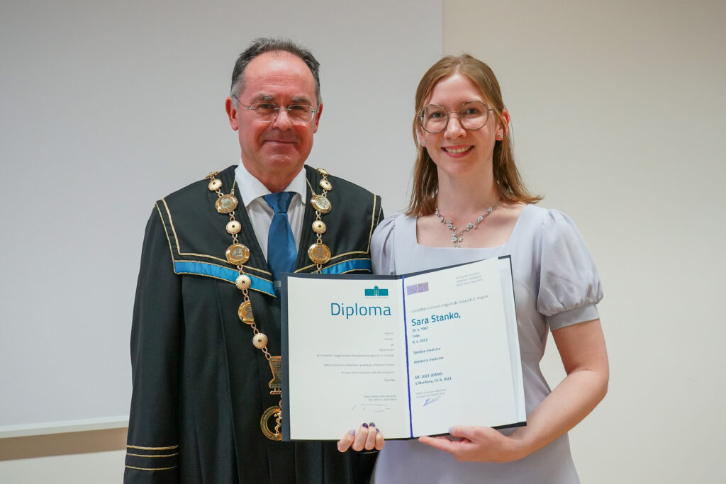 Diplomantka v svetlo sivi obleki z dekanom in diplomo. Podelitev diplom Medicinske fakultete UM, 15. junija 2023.