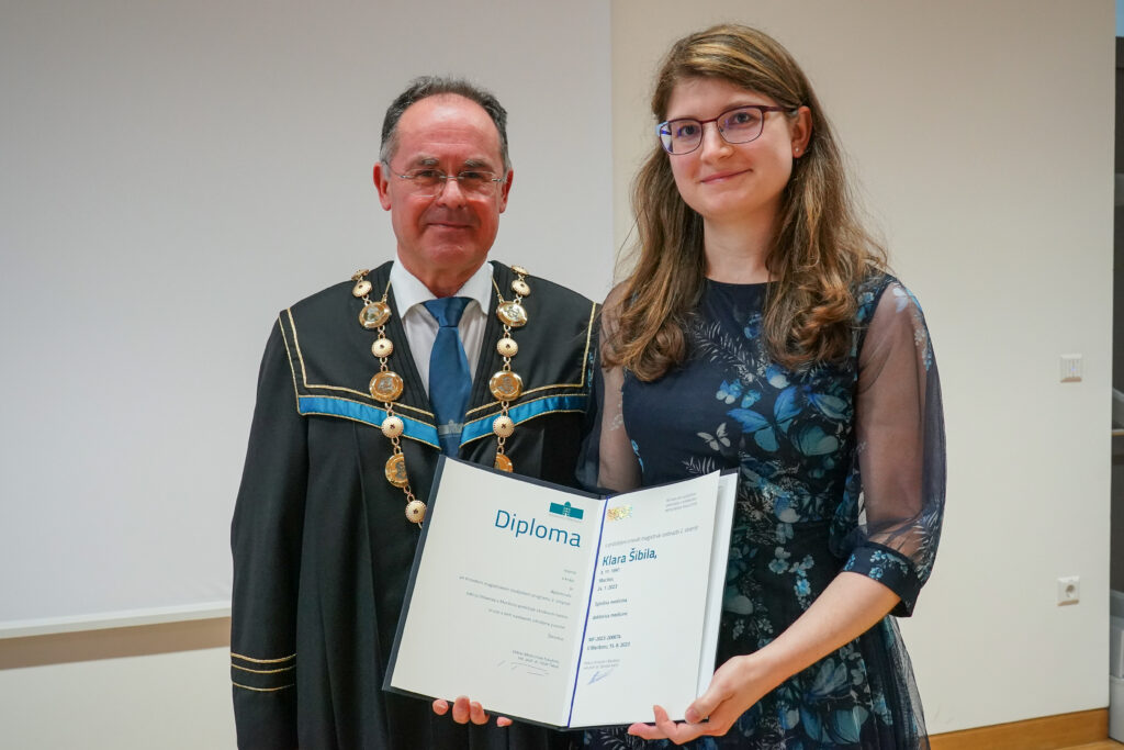 Diplomantka v modri obleki z dekanom in odprto diplomo. Podelitev diplom Medicinske fakultete UM, 15. junija 2023.