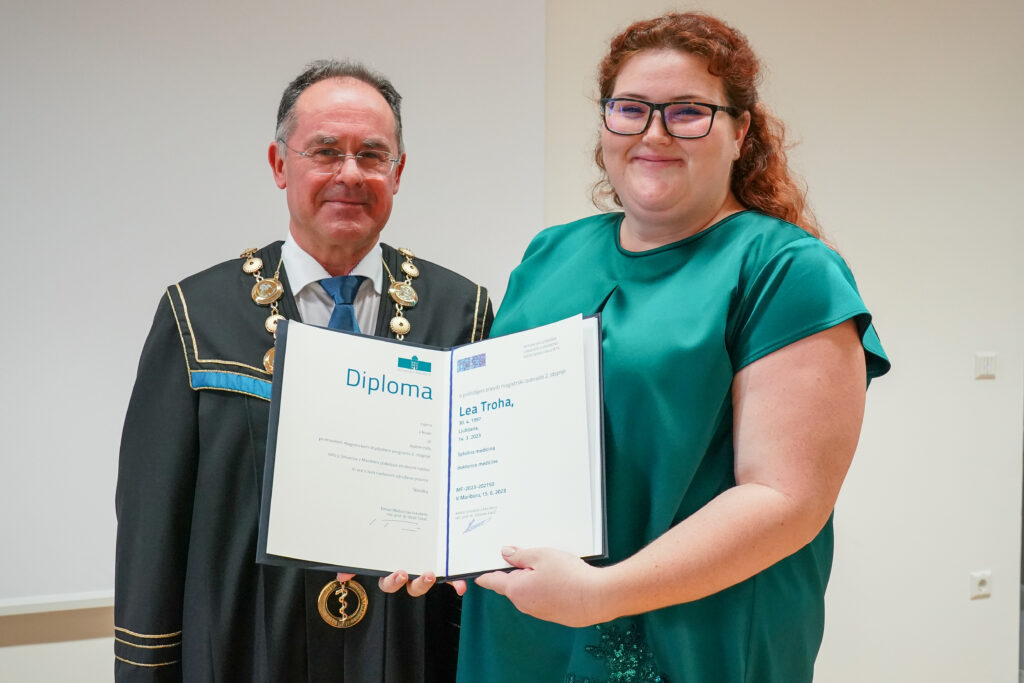 Diplomantka v zeleni obleki z dekanom in diplomo. Podelitev diplom Medicinske fakultete UM, 15. junija 2023.