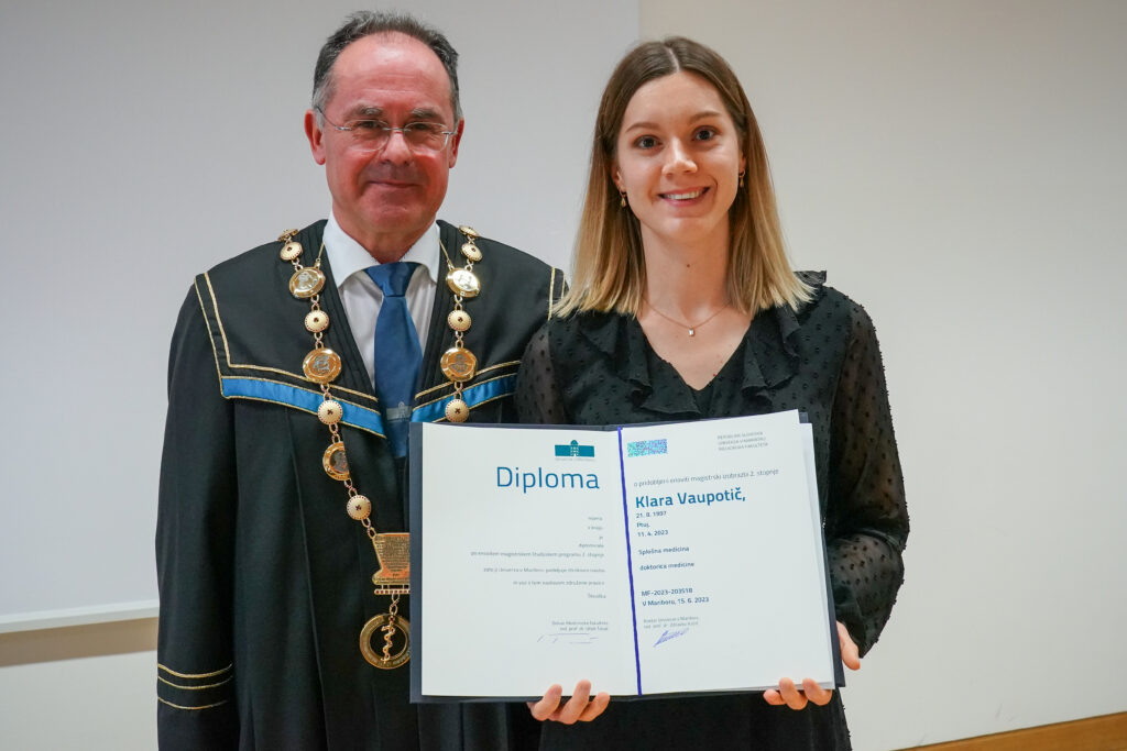 Diplomantka v črnem z dekanom in odprto diplomo. Podelitev diplom Medicinske fakultete UM, 15. junija 2023.
