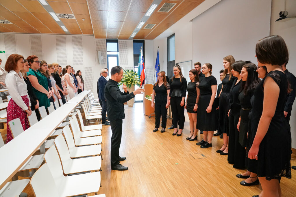 Diplomanti stoje poslušajo nastop pevskega zbora. Podelitev diplom Medicinske fakultete UM.