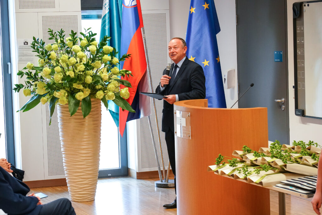 Povezovalec z mikrofonom ob zastavah in šopkih. Podelitev diplom Medicinske fakultete UM.