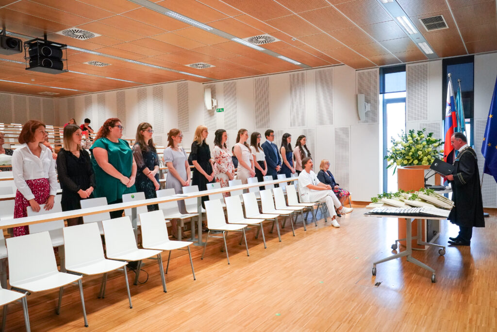 Diplomanti in gostje stojijo ob klopeh v predavalnici. Podelitev diplom Medicinske fakultete UM, 15. junija 2023.