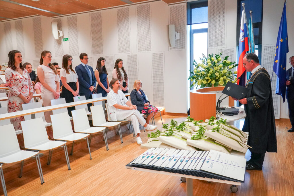Dekan nagovarja diplomante, ki stojijo ob klopeh. Podelitev diplom Medicinske fakultete UM, 15. junija 2023.