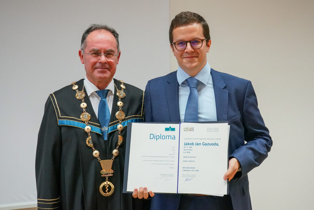 Diplomant v modri obleki z dekanom in diplomo. Podelitev diplom Medicinske fakultete UM, 15. junija 2023.