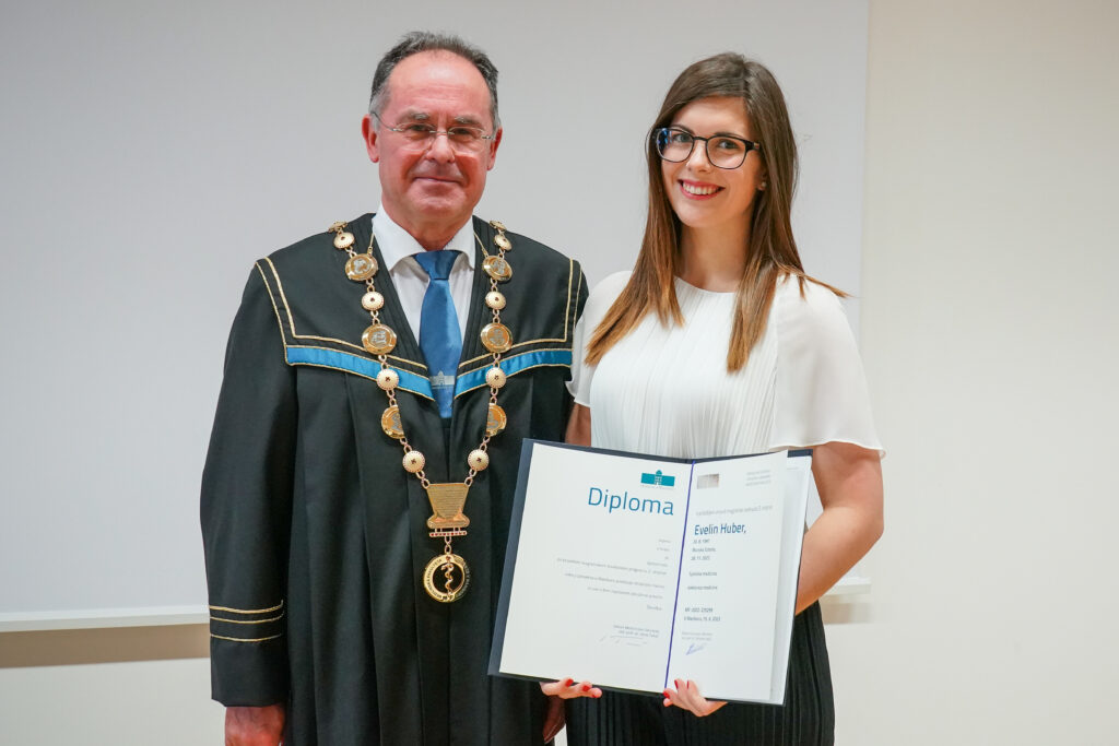 Diplomantka v beli majici z dekanom in diplomo. Podelitev diplom Medicinske fakultete UM, 15. junija 2023.