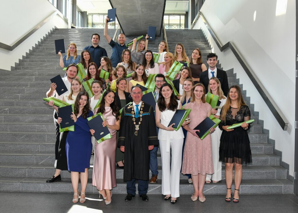 Gruppenfoto der Absolventinnen und Absolventen mit Blumensträußen auf der Treppe. Diplomverleihung der MF UM 2025.